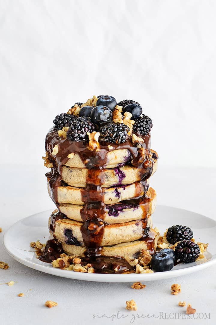 Eye-level shot of the Blueberry Oat Pancakes, Topped with blackberries, blueberries, crushed walnuts and chocolate sauce.