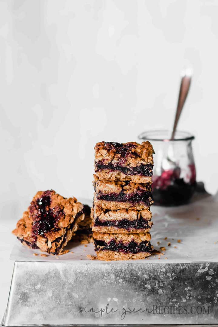 Eye-level shot of the Breakfast Blueberry Oatmeal Bars stack with the blueberry jam jar behind.