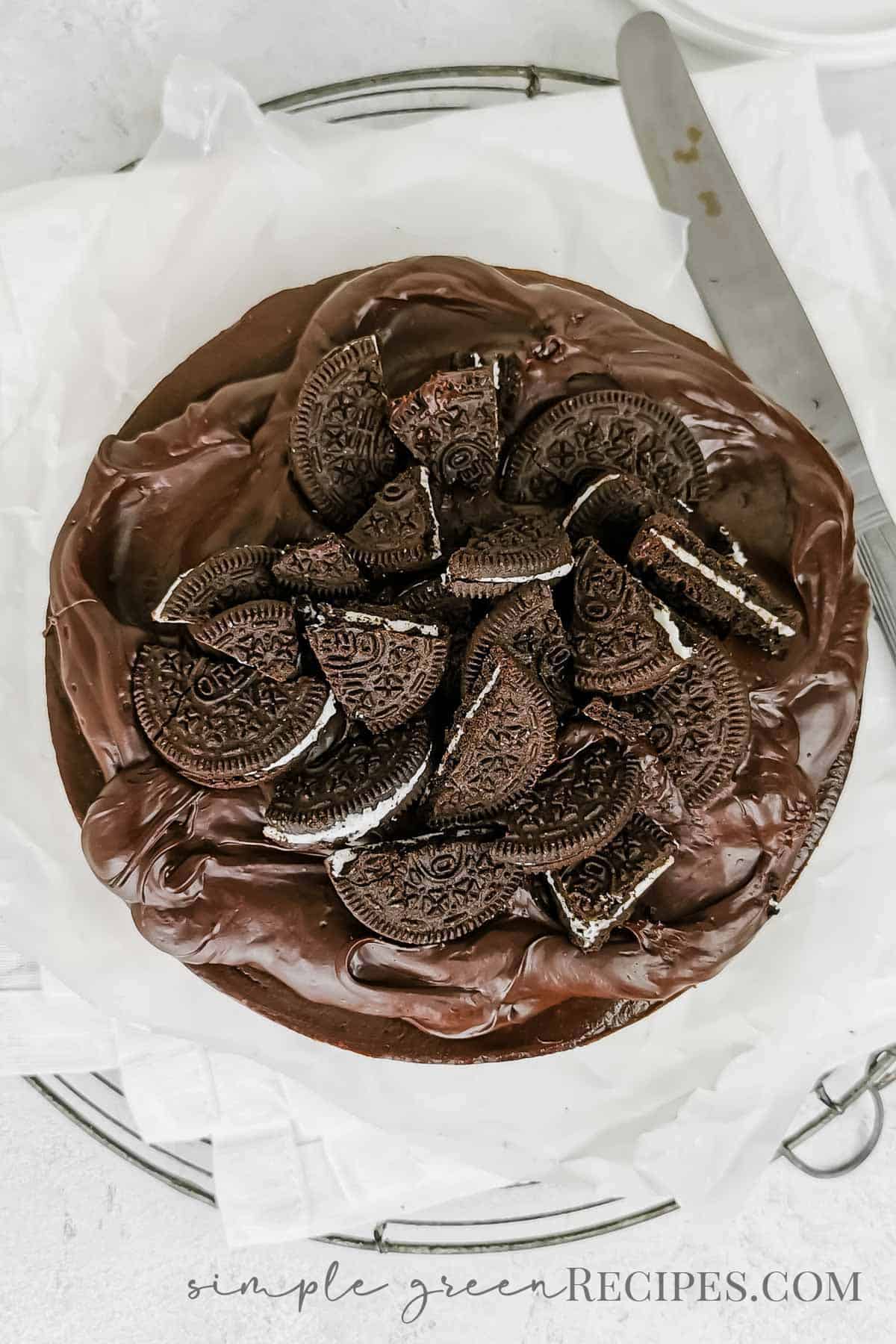 Uncut cheesecake made up of a cookie crust, chocolate cheesecake and topped with ganache and extra cookies.
