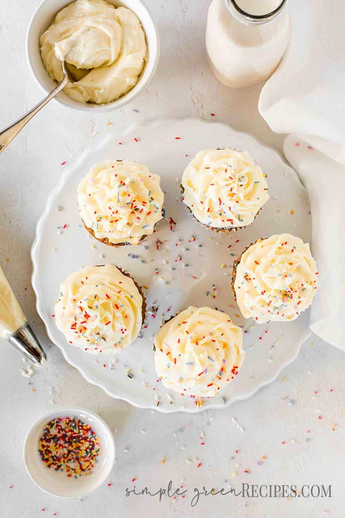 Cupcakes frosted with vanilla buttercream and topped with colourful sprinkles, on a white surface