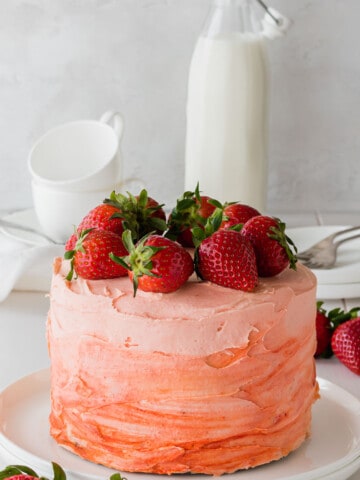 uncut strawberry cake on a white plate topped with fresh strawberries.