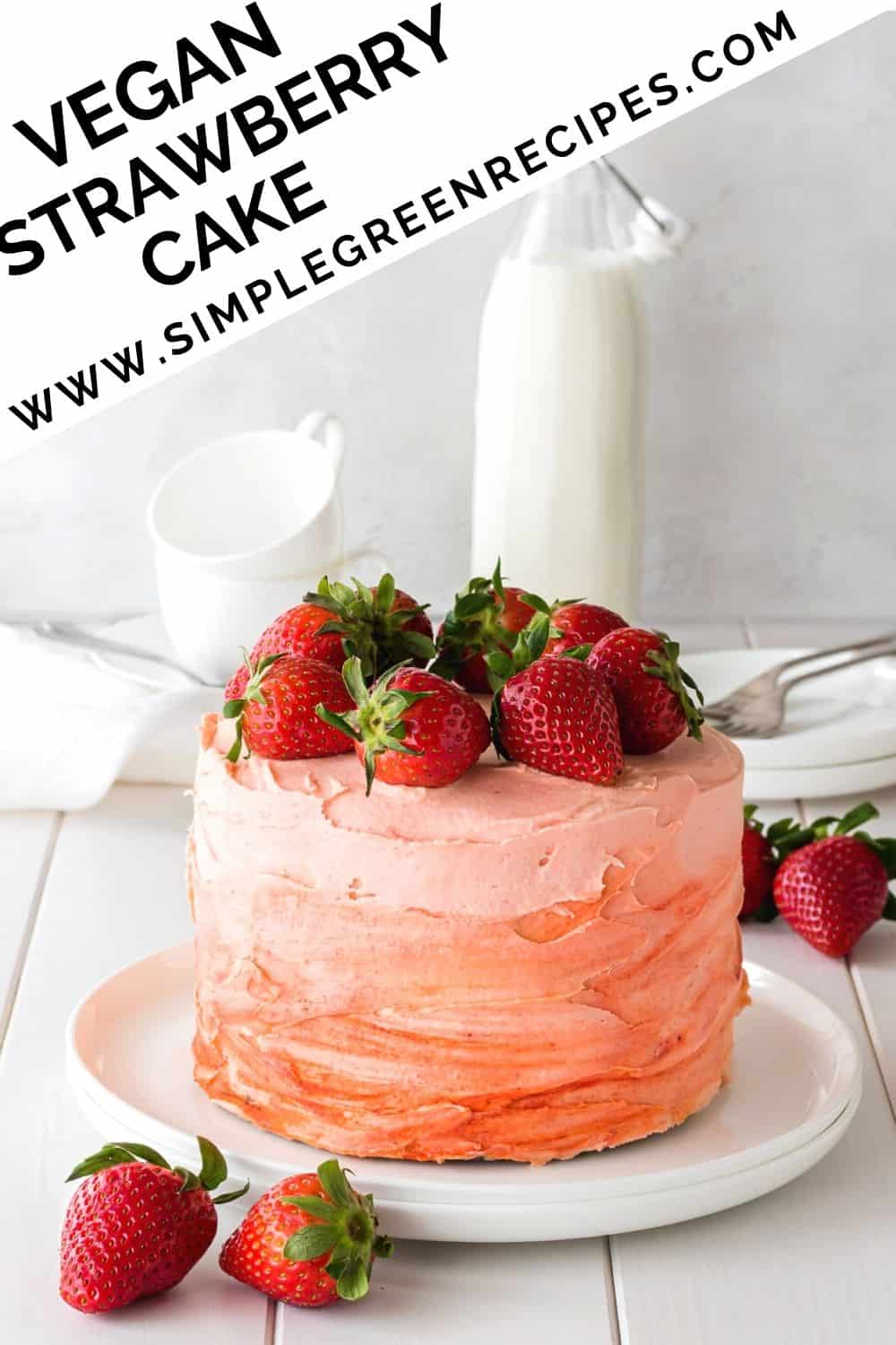 Strawberry cake on a white plate, topped with fresh strawberries, in front of a milk bottle.