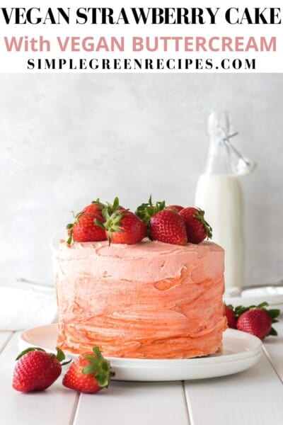 Strawberry cake on a white plate, topped with fresh strawberries, in front of a milk bottle.