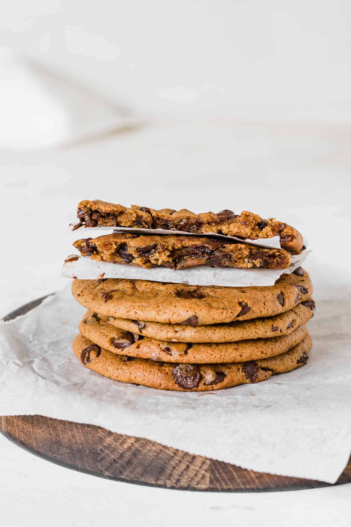 Stack of chocolate chip cookies on a parchment paper, with a cookie on top split in two