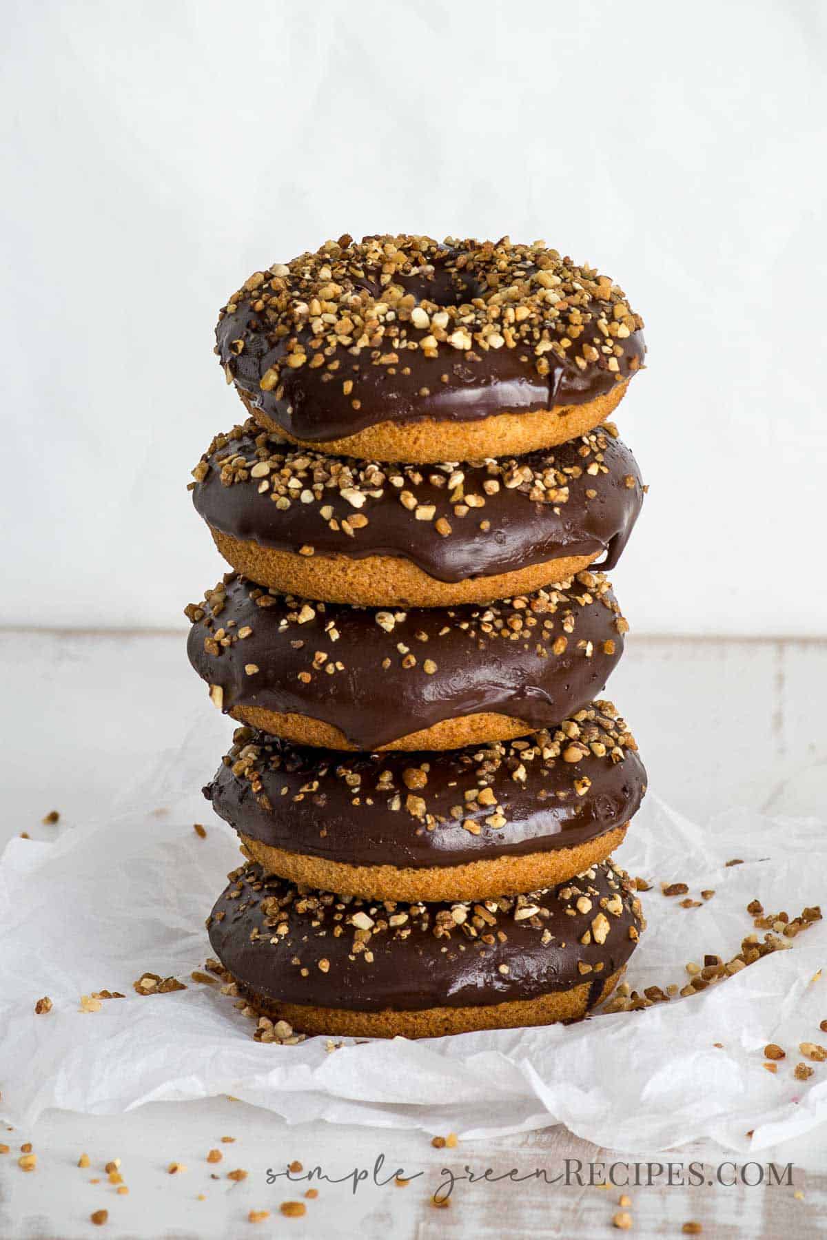 stack of donuts, frosted with glaze chocolate and crunchy almonds, on a parchment paper