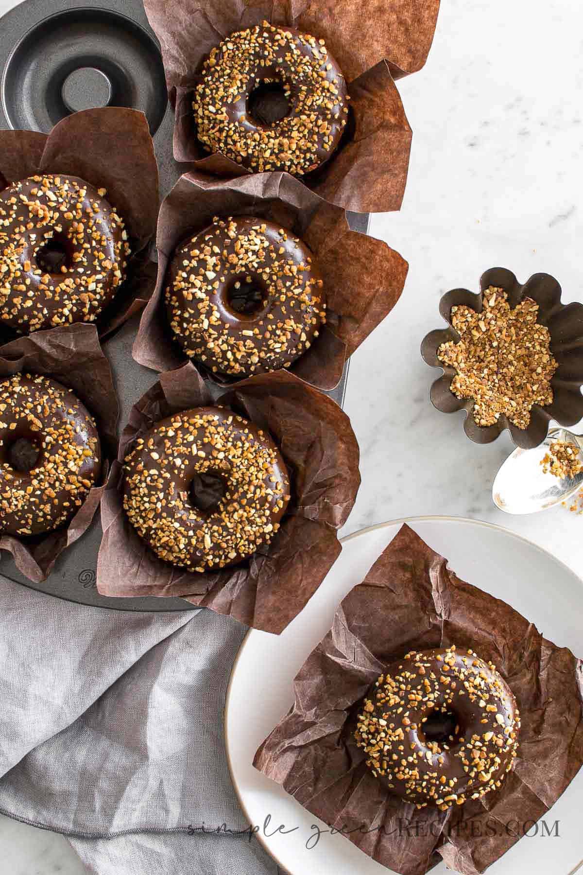 6 donuts frosted with glaze chocolate and crunchy almonds, on a brown muffin paper