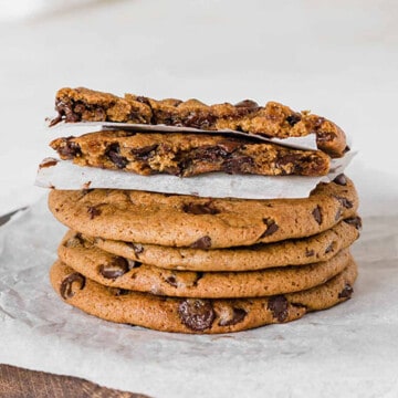 Stack of chocolate chip cookies on a parchment paper, with a cookie on top split in two