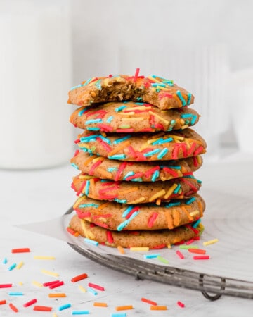 Stack of cookies with sprinkles on a parchment paper over a cooling rack