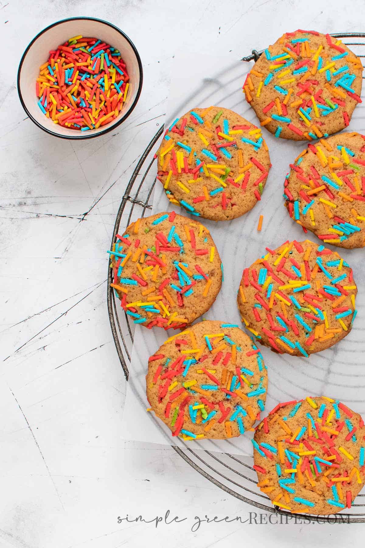 Sprinkle Cookies on a round cooling rack and a bowl full of colourful sprinkles