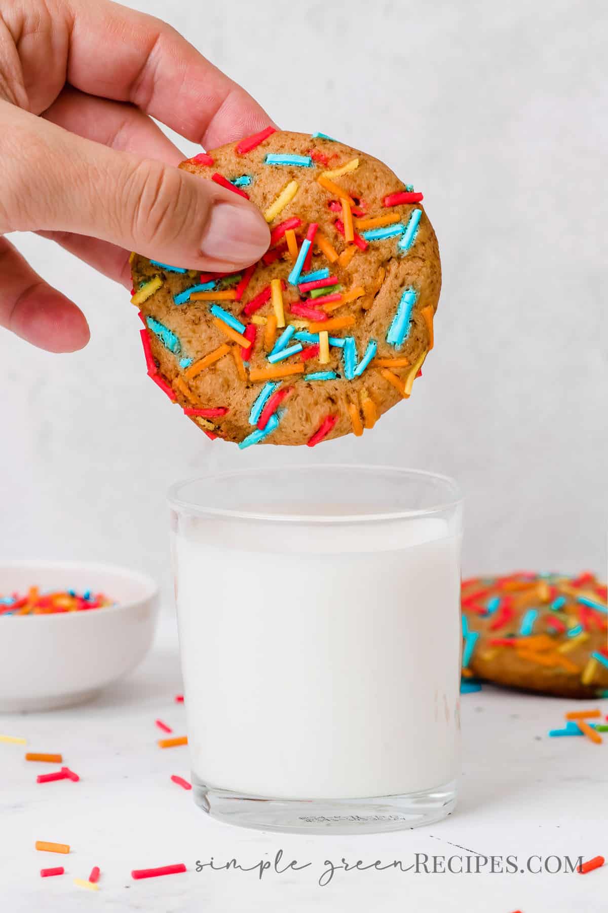 Hand holding a sprinkle cookie over a glass of milk