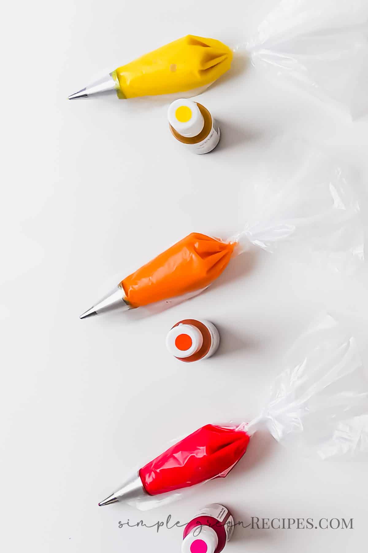 Three piping bags fitted with piping tips and filled with red, orange and yellow icing, and three bottles of food coloring.