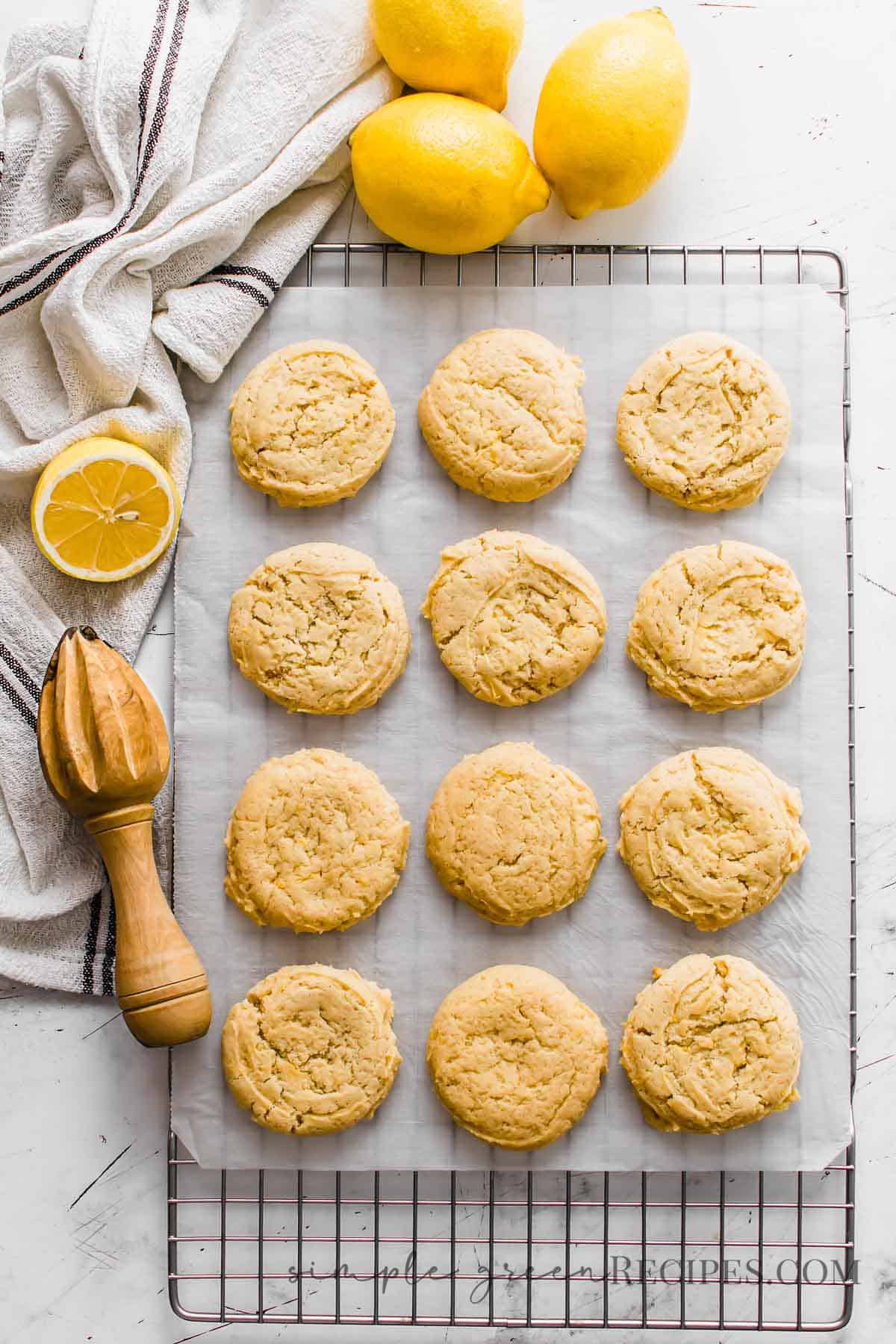 Cookies on a parchment paper over a cooling rack, surrounded by lemons, a dish towel and a wooden squeezer.