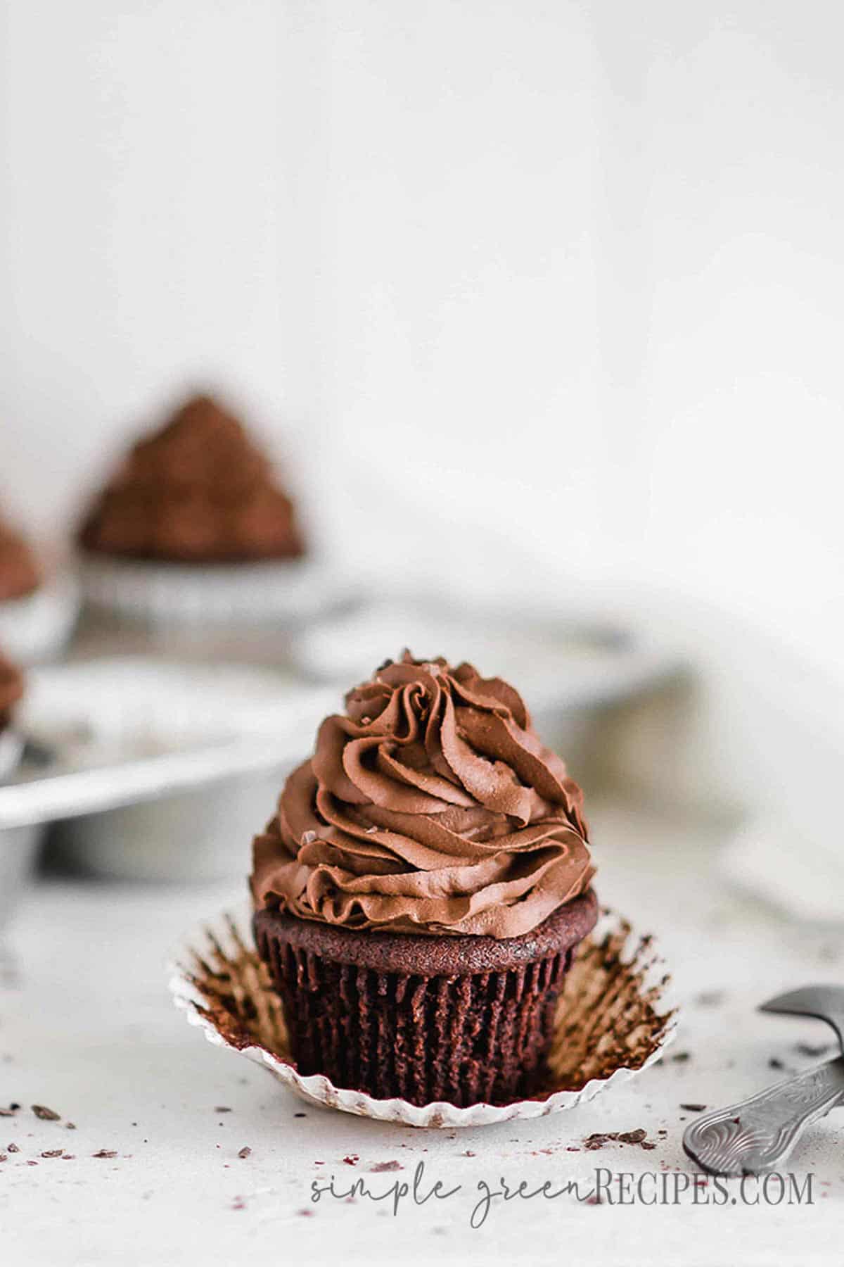 Cupcake muffin peeled on a white surface, next to a grey spoon and a pan with cupcakes.