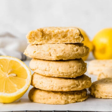 Stack of cookies next to a halved lemon, placed on a parchment paper over a cooling rack.