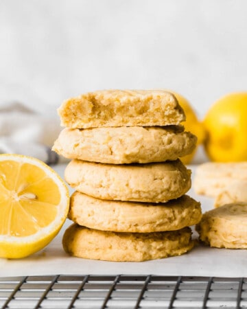 Stack of cookies next to a halved lemon, placed on a parchment paper over a cooling rack.