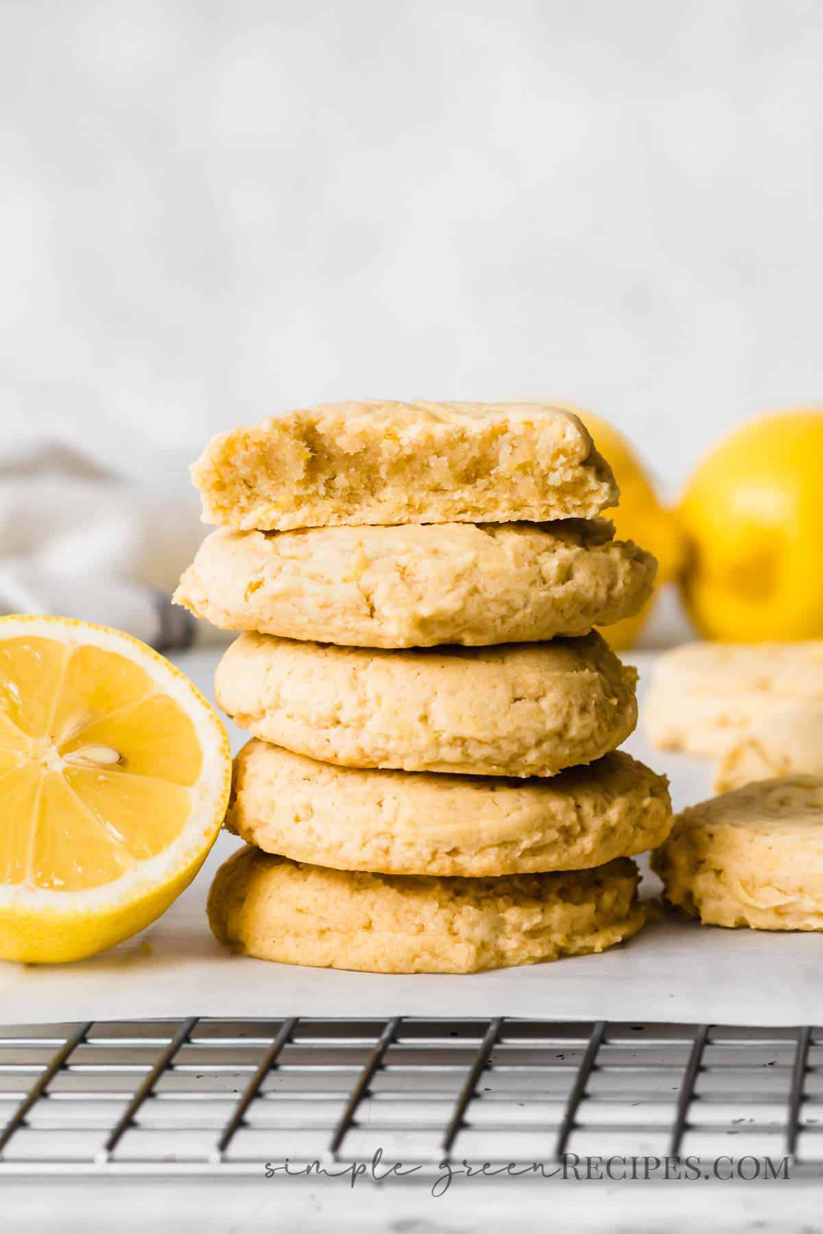 Stack of cookies next to a halved lemon, placed on a parchment paper over a cooling rack.