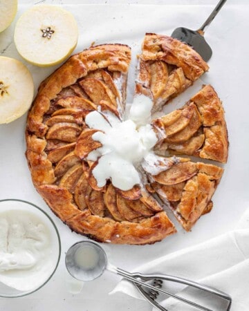 sliced apple galette on a white surface, halved apples, bowl with ice cream and ice cream scoop.