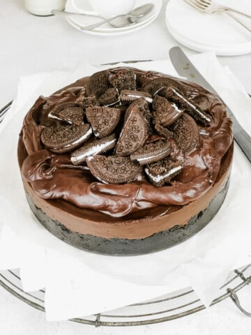 chocolate cheesecake topped with oreo cookies, against a white surface.