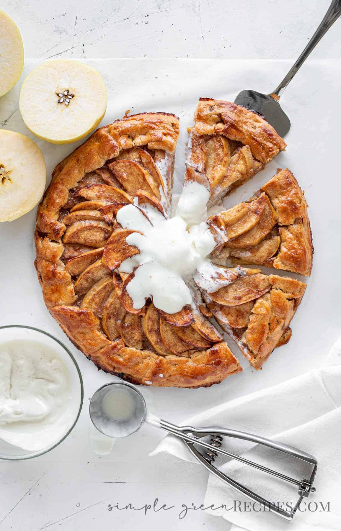 cut apple galette with ice cream on top, on a white surface