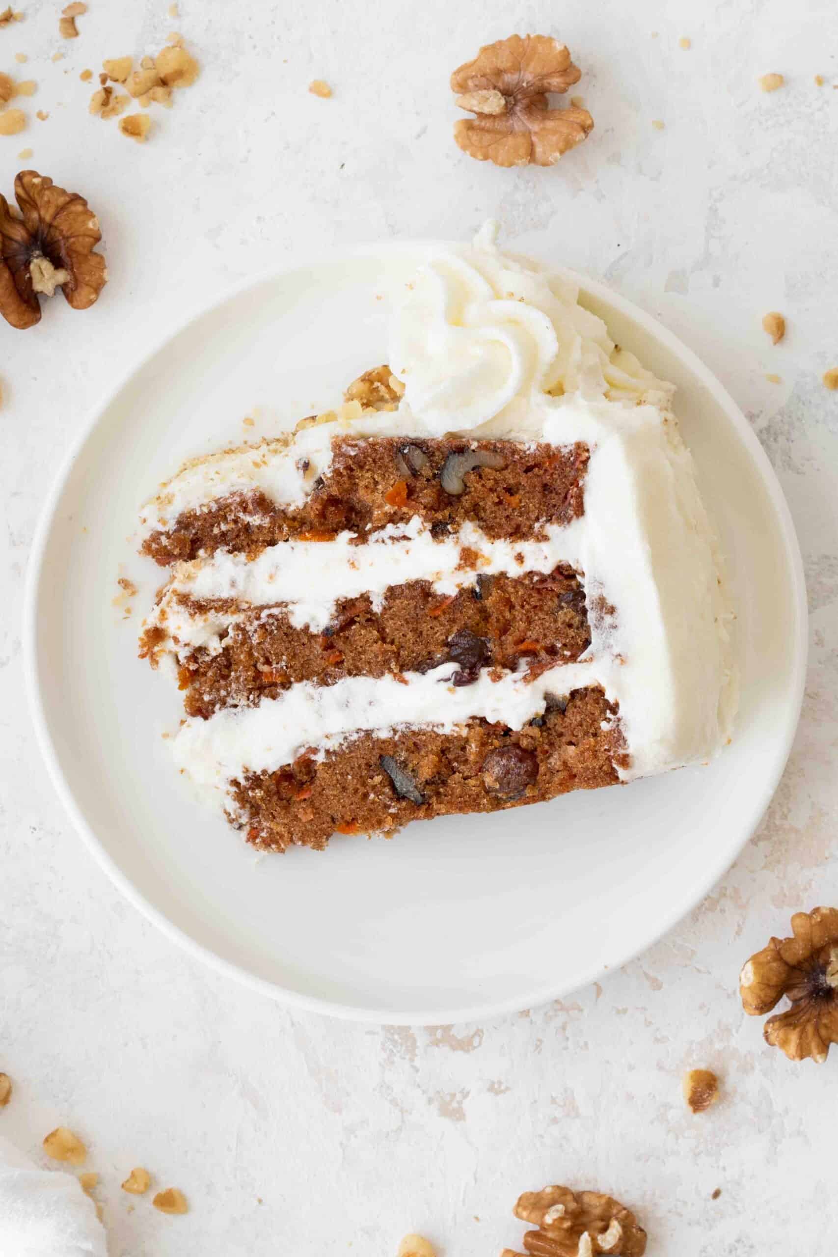 slice of frosted carrot cake on a white plate, on a white surface